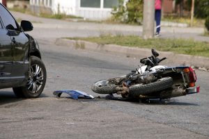 A motorcycle lies damaged on the road next to a damaged car.