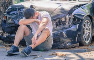 man cries in front of wrecked car