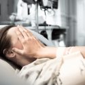 stressed woman holds head while lying in hospital bed