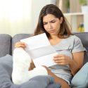 woman in leg cast frowns at medical bills.