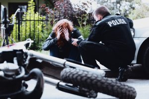 policeman consoles woman with wrecked motorcycle in foreground