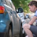 A man looking at damage to his car and wondering how to file a report for a hit-and-run in Georgia.