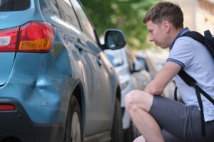 A man looking at damage to his car and wondering how to file a report for a hit-and-run in Georgia.
